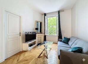A living room with a sofa, a glass coffee table, a television, and a window with curtains. - Apartment near Montmartre (Paris)