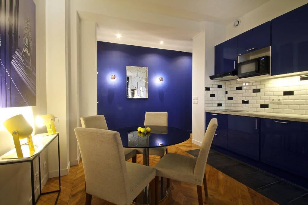 Una cocina moderna con armarios azules, un microondas y una zona de comedor con una mesa y sillas de vidrio.
