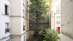 A narrow urban courtyard with buildings on either side, a tree in the center, and a small garden area. - Apartment near Montmartre (Paris)