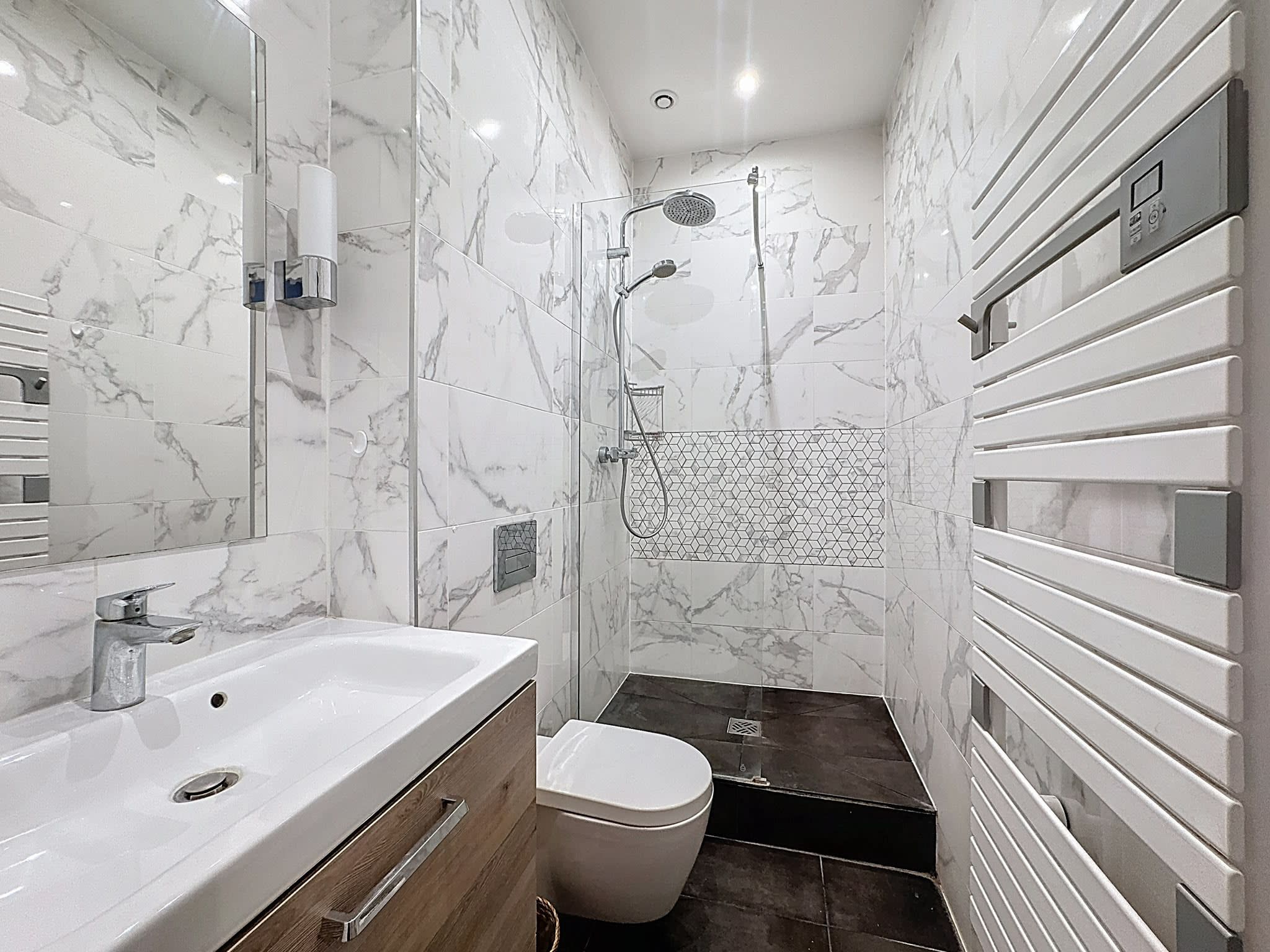 Une salle de bain moderne avec un mur en marbre, une douche, des toilettes et un lavabo.