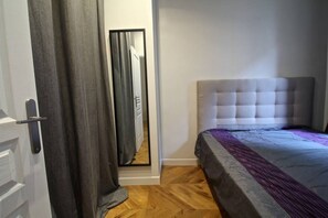 A bedroom with a bed, a mirror, a door, and a wooden floor. - Apartment near Montmartre (Paris)