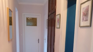 A narrow hallway with a bench on the left, a door at the end, and a blue wall on the right. - Modern cocoon with garden and beautiful sea view (Cavalaire-sur-Mer)