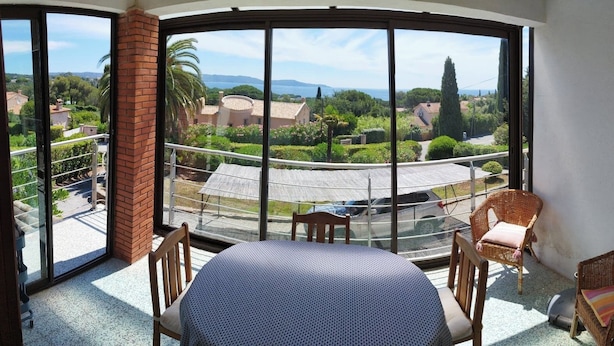 A balcony with a view of a residential area, a table, and two wicker chairs. - Modern cocoon with garden and beautiful sea view (Cavalaire-sur-Mer)
