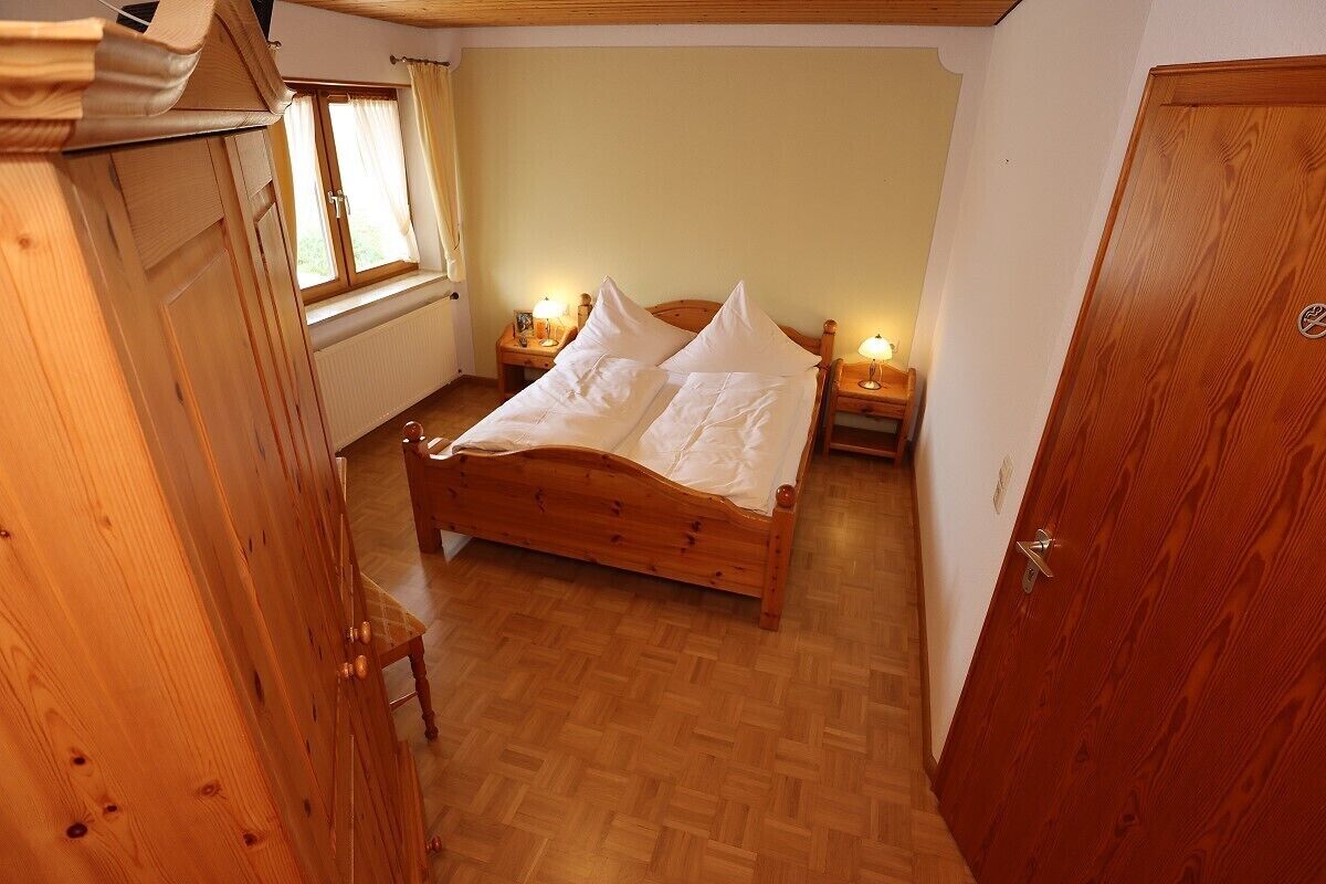 A wooden bed with white bedding in a room with wooden floors and a window.