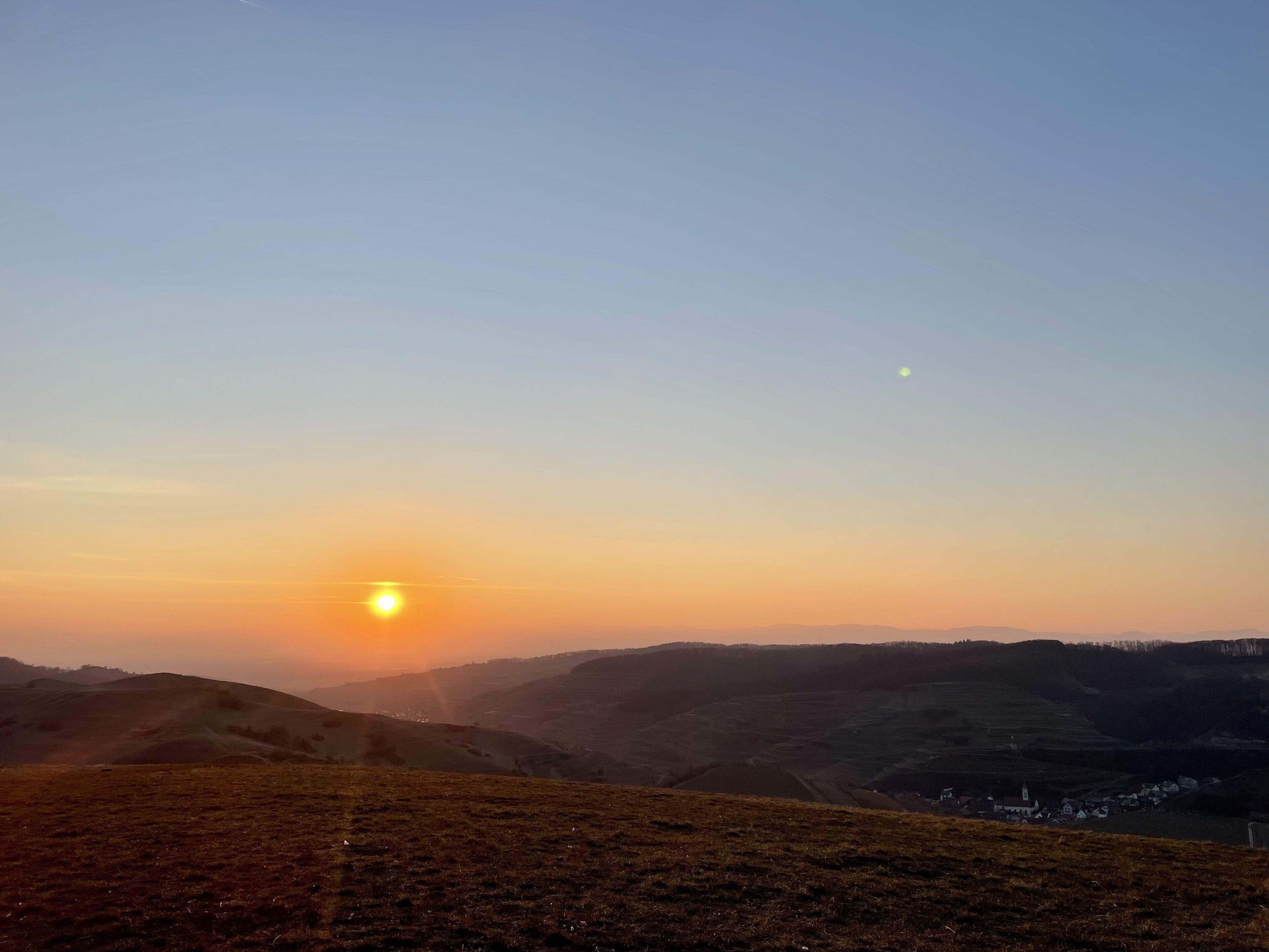 Eine Landschaft mit sanften Hügeln und einer kleinen Siedlung im Tal.