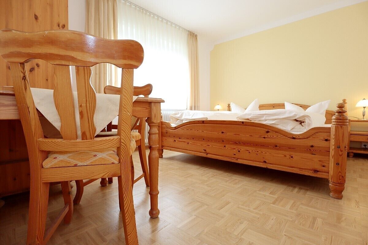 Una cama de madera en una habitación con una silla de madera y una mesita.
