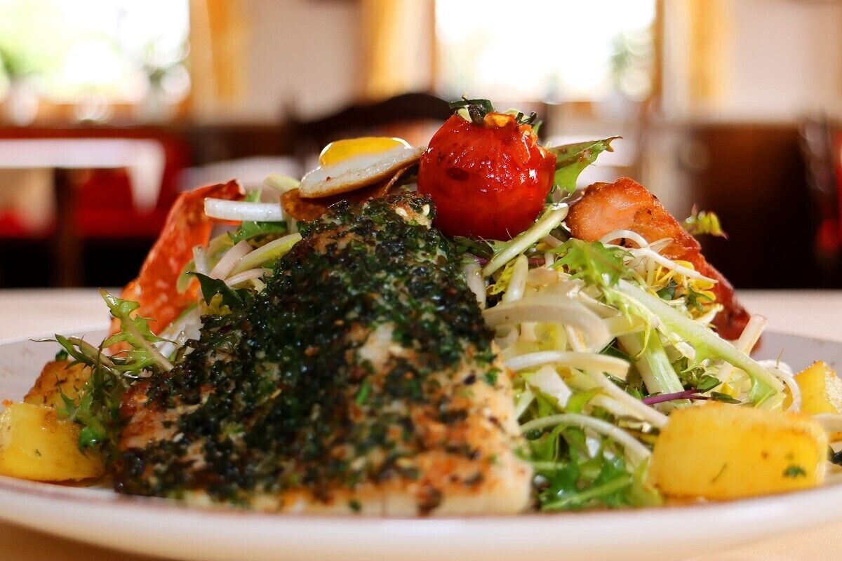 A plate of food with a fish fillet, vegetables, and a cherry tomato.