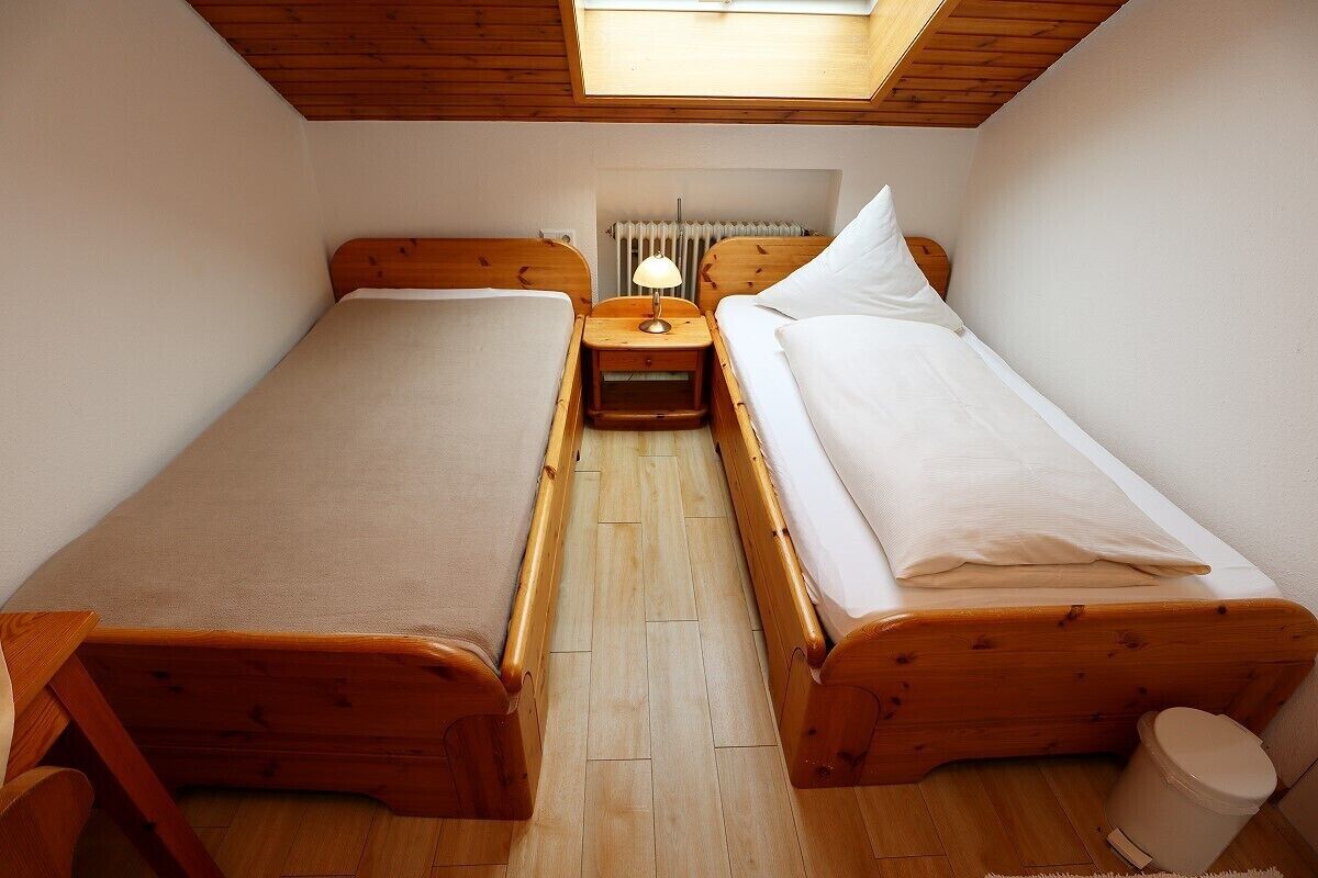 Una habitación pequeña y acogedora con dos camas de madera, una mesita de noche con lámpara y un radiador.