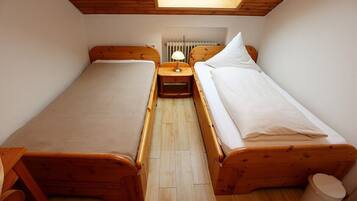 Una habitación pequeña y acogedora con dos camas de madera, una mesita de noche con lámpara y un radiador.