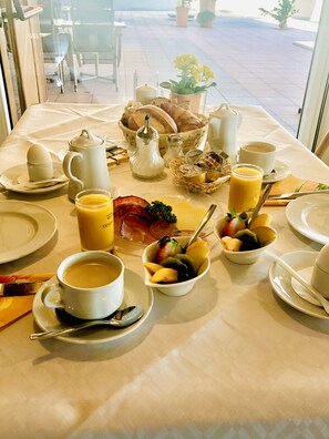 Ein Frühstückstisch reichhaltig gedeckt mit verschiedenen Speisen, darunter Eier, Brot, Obst und Getränke.