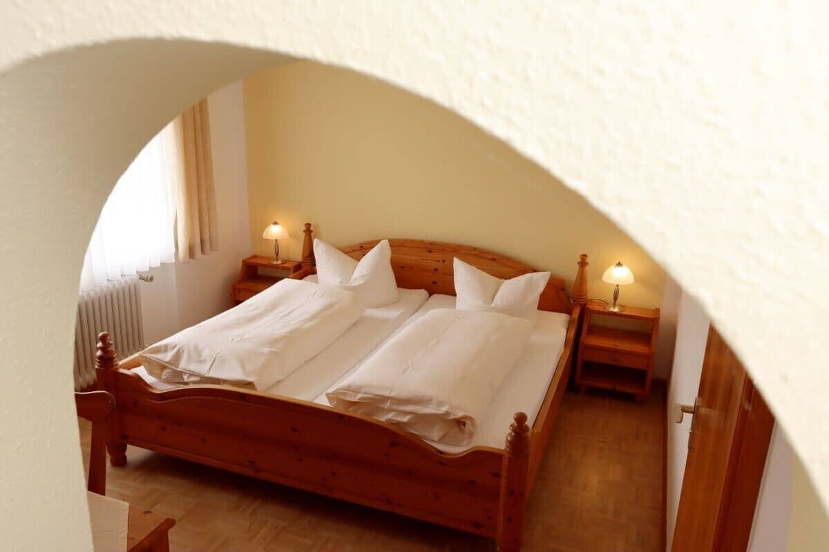 A neatly made double bed with white linens, two bedside tables with lamps, and a wooden headboard.