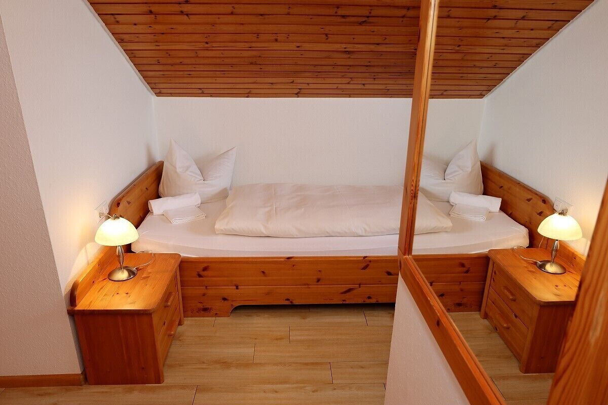 Ein kleines, gemütliches Schlafzimmer mit Holzbalkendecke und zwei Nachttischen mit Lampen.