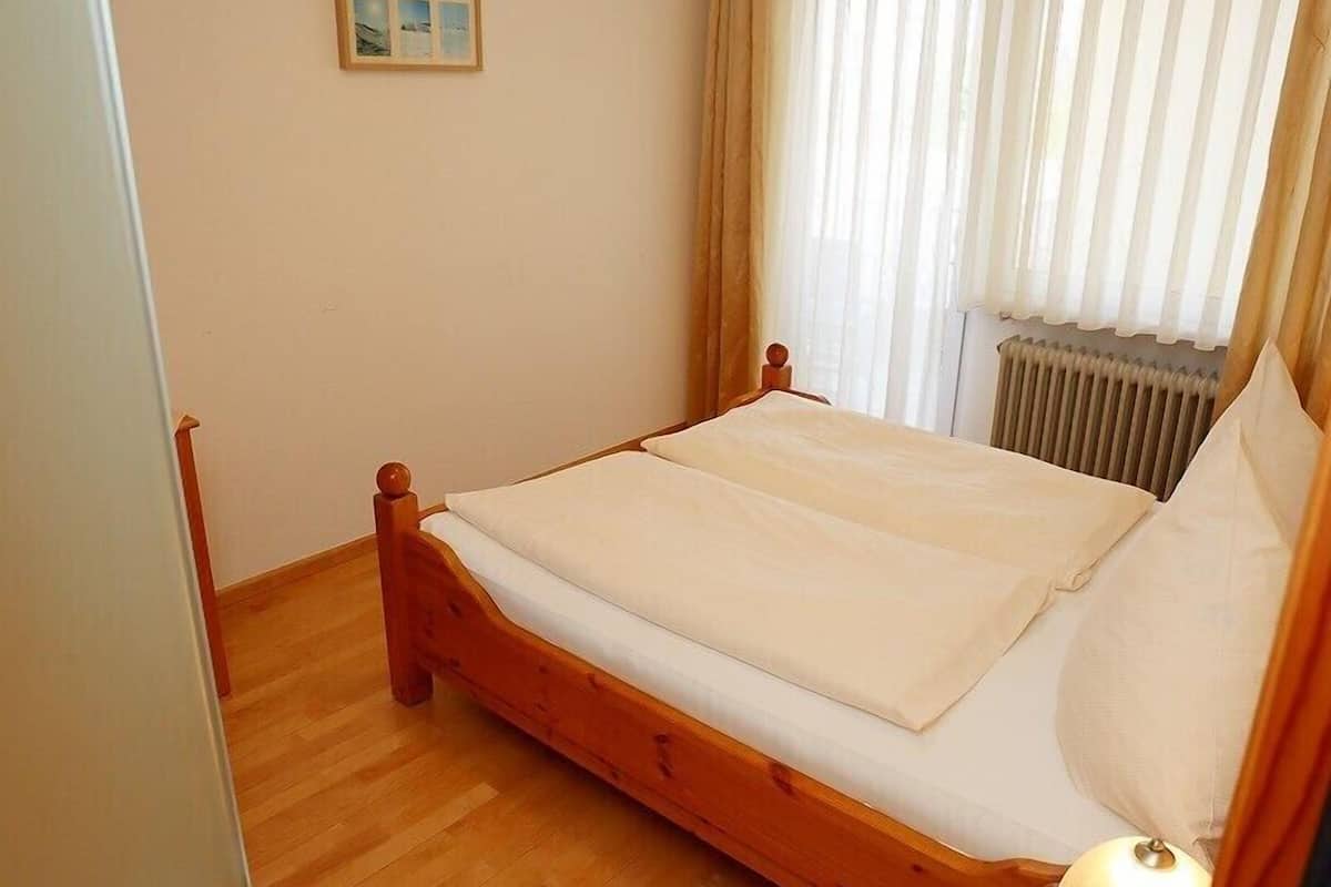 A bedroom with a wooden bed, a bedside table with a lamp, a radiator, and a window with curtains.