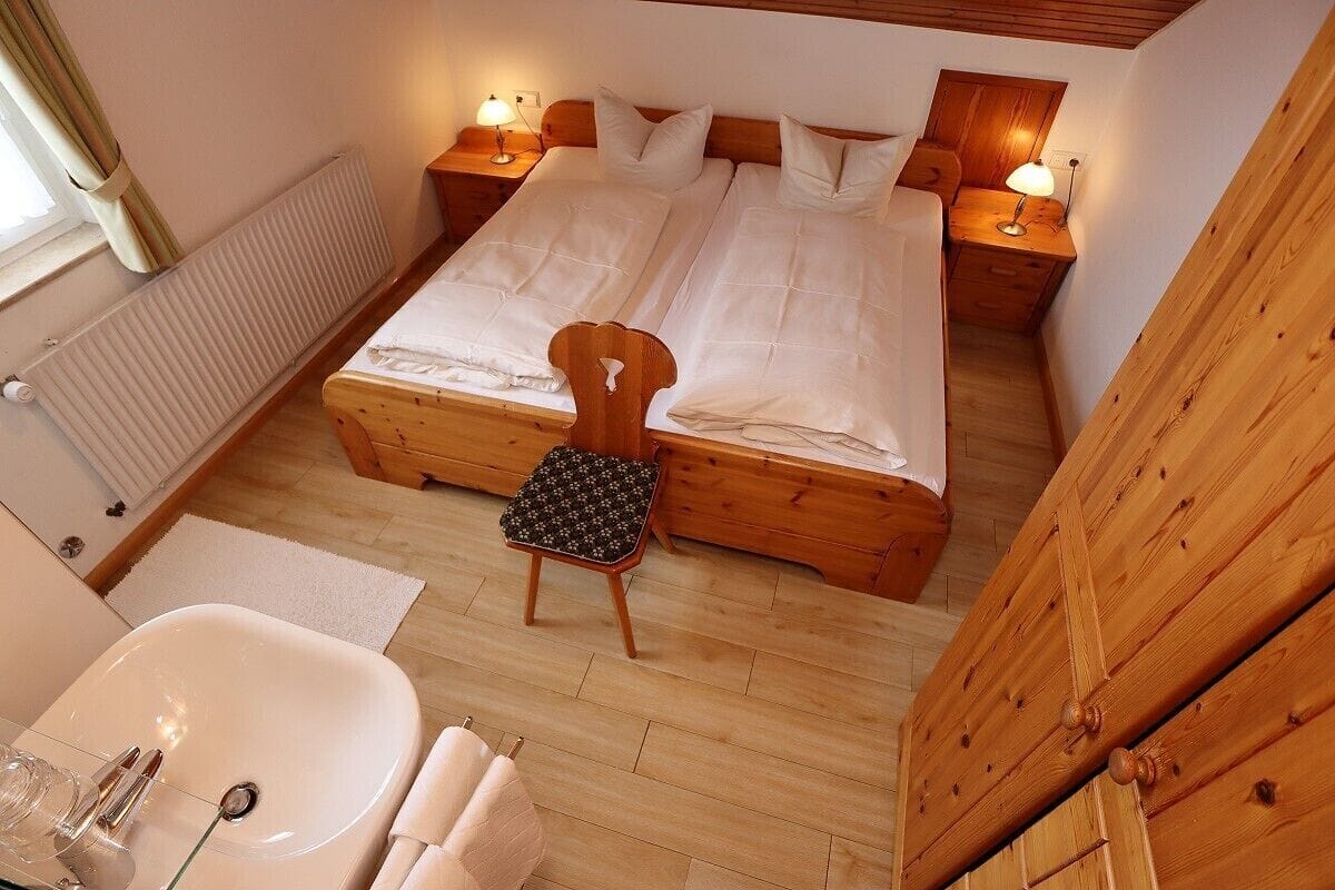 A bedroom with two beds, a wooden floor, a radiator, a bedside table with a lamp, and a chair.