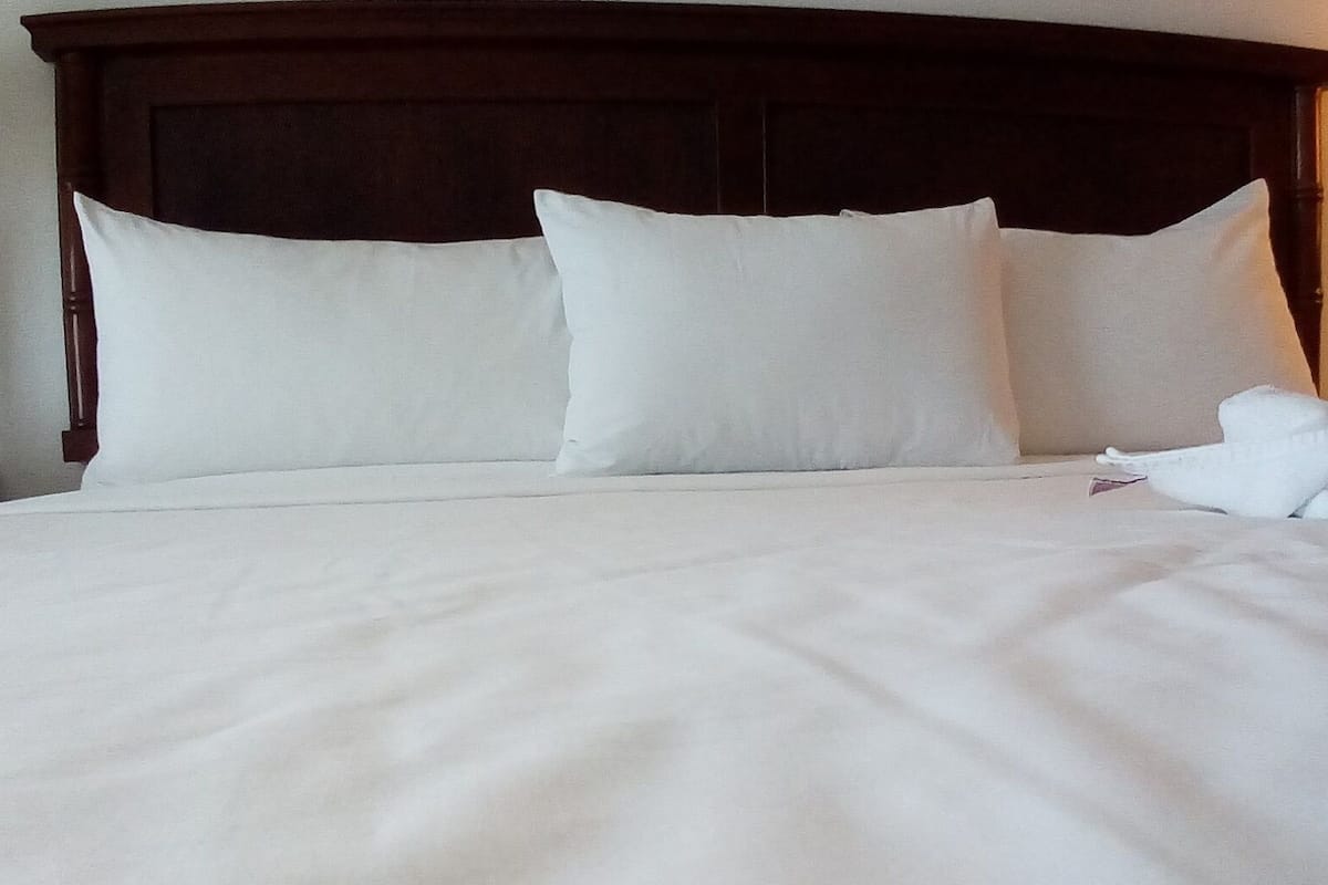 A neatly made bed with white linens and pillows, a wooden headboard, and a white towel on the side.