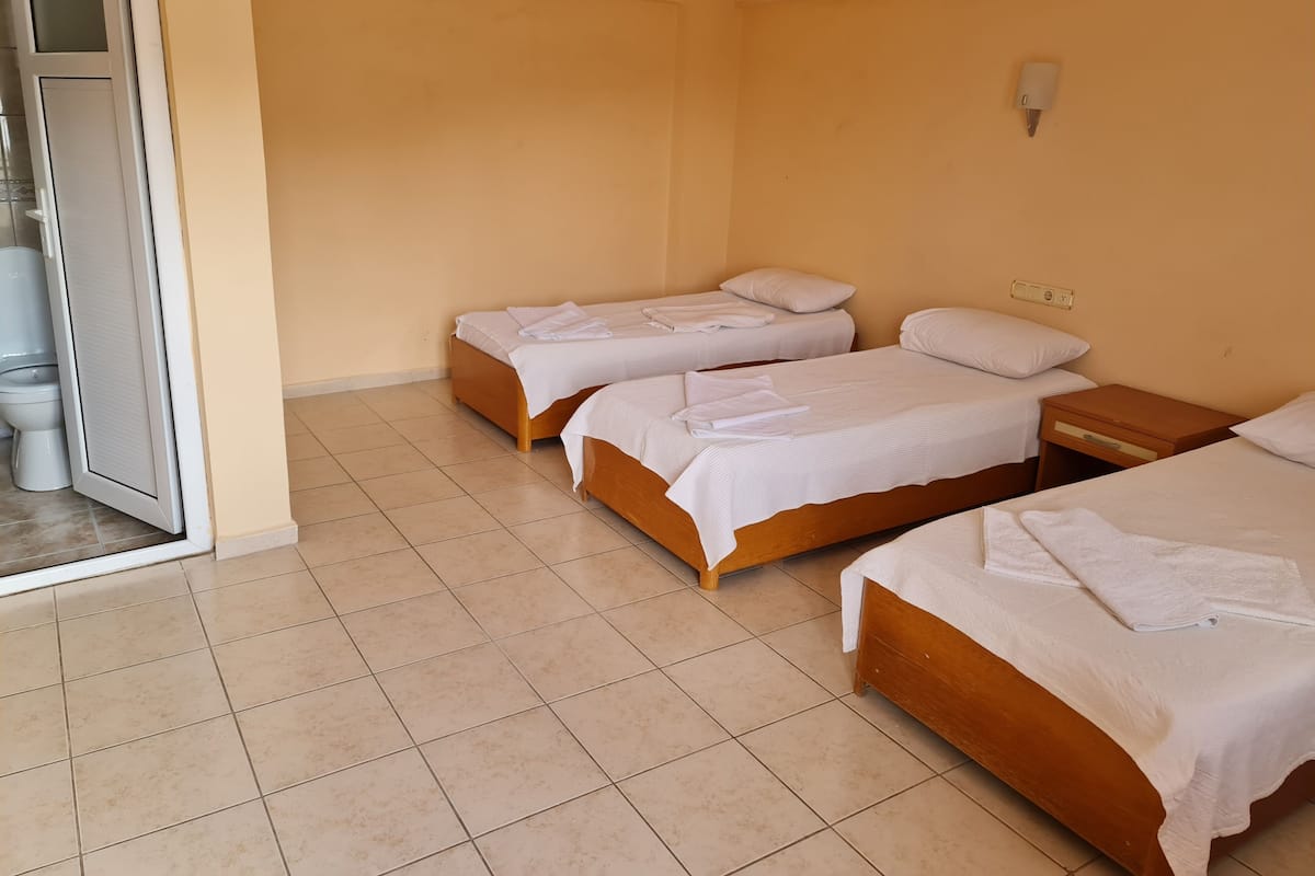 A hotel room with three single beds, a bathroom with a toilet and sink, and a sliding glass door to the outside.