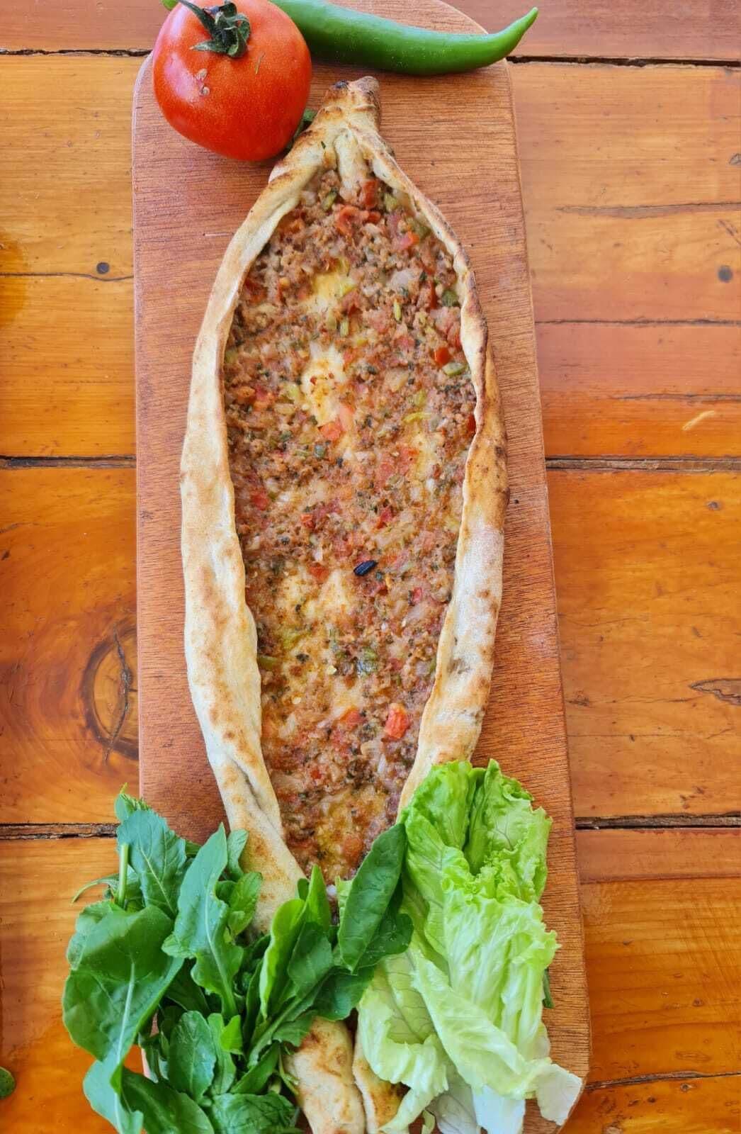 A flatbread with a savory filling, accompanied by a tomato and a green chili, and garnished with fresh greens.