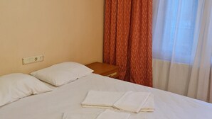 A hotel room with a bed, white linens, a wooden nightstand, a power outlet, and a window with curtains. - CANER MOUNTAIN HOTEL (Kemer)