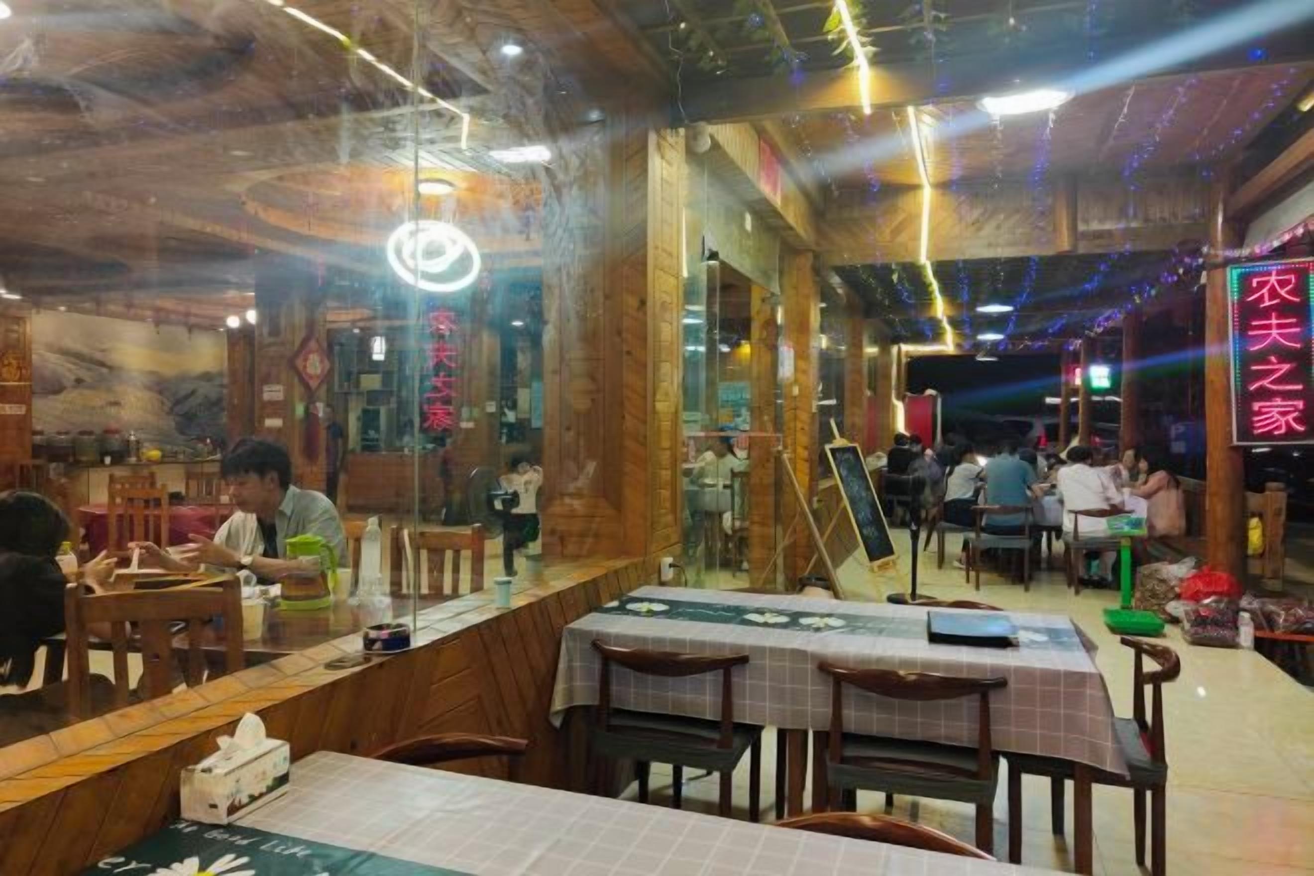 Interior de restaurante con mesas y sillas de madera, una barra y letreros de neón.
