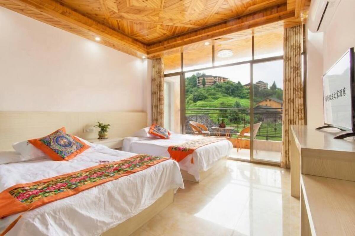 Une chambre d’hôtel avec deux lits, une télévision et une vue sur un paysage verdoyant.