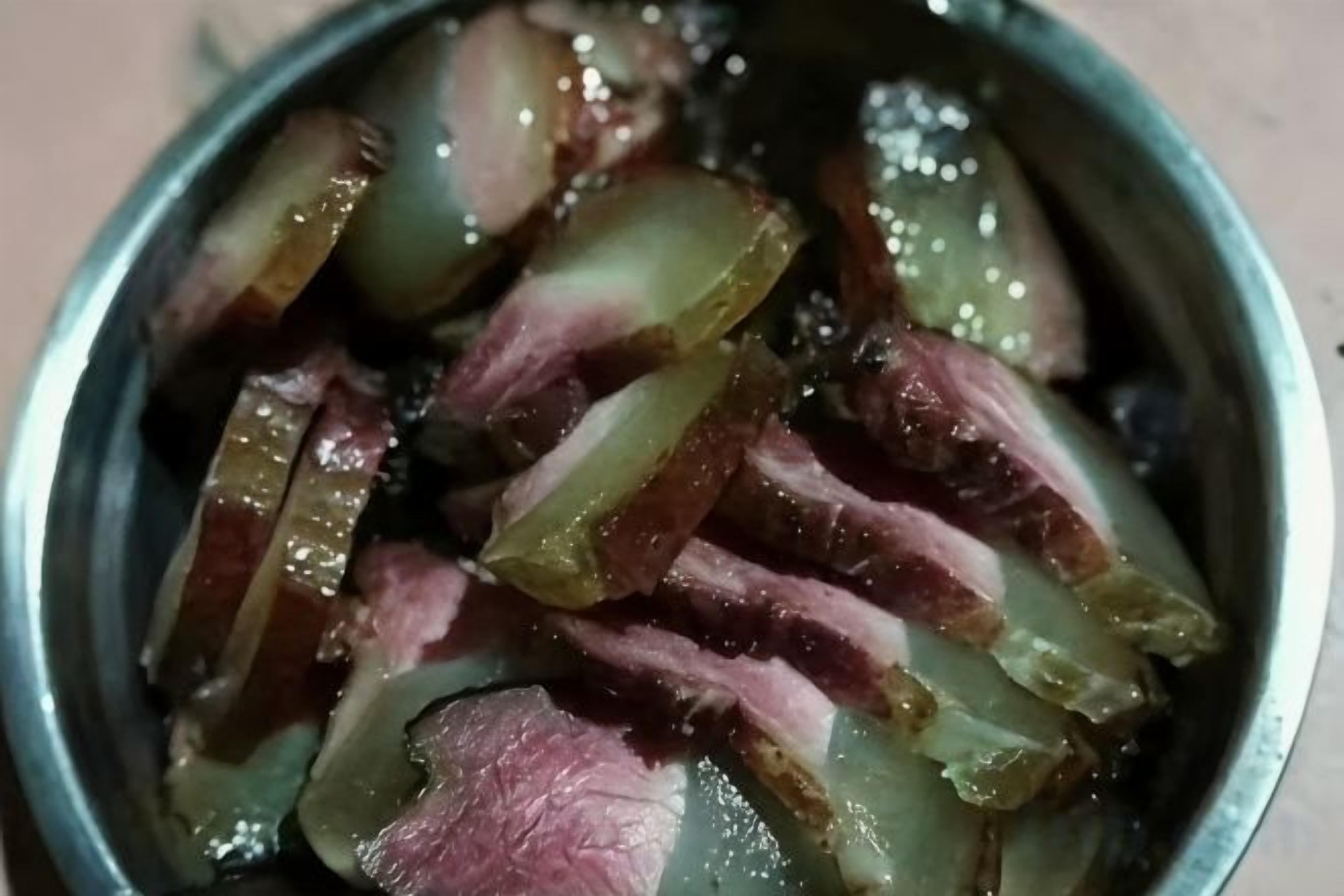 Un bol en métal contenant de la viande coupée en tranches et des oignons.