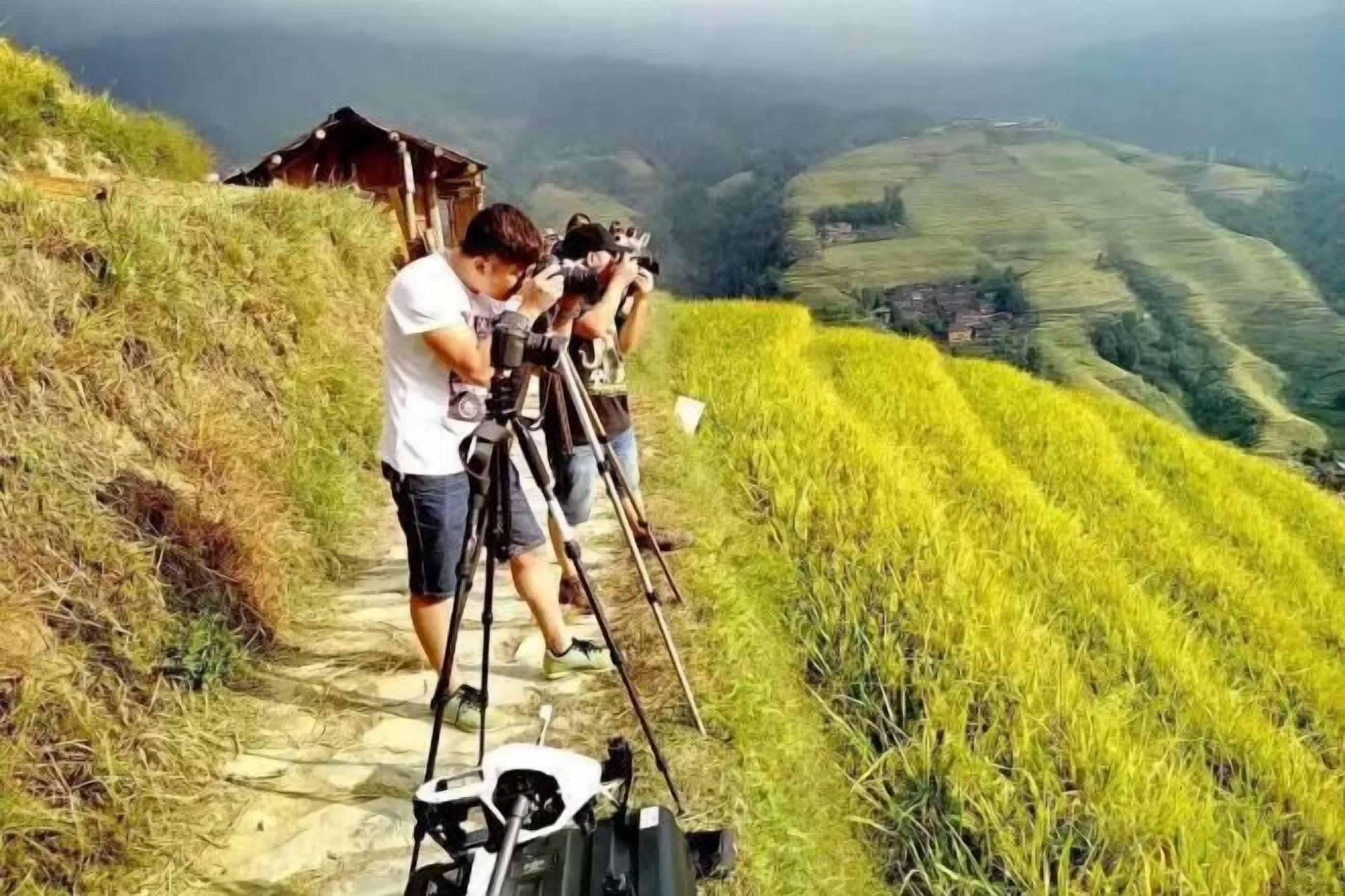 A person setting up a camera on a path with a rural landscape in the background.