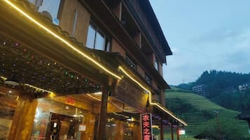 A traditional building with a wooden facade, a signboard, and a view of a green hillside.
