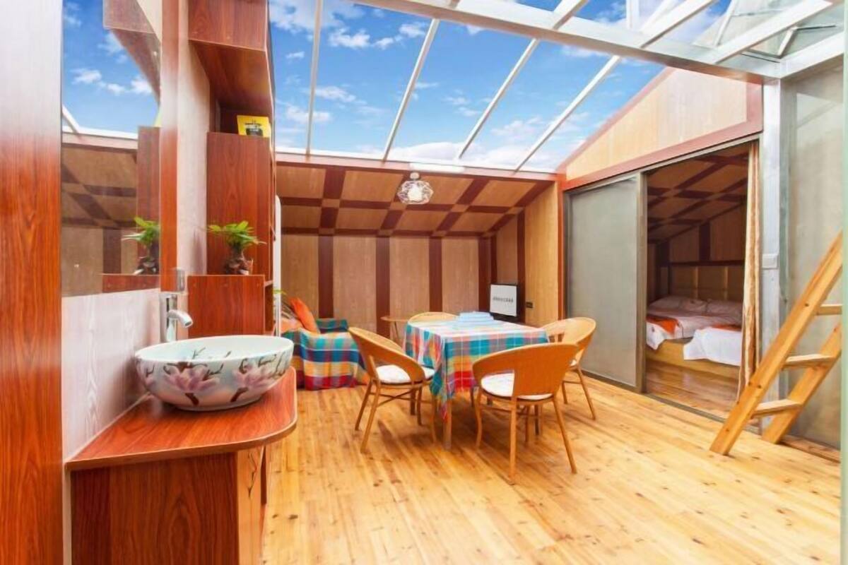 Une pièce de taille modeste, avec un plancher en bois, une table et des chaises, un petit lavabo et un lit.
