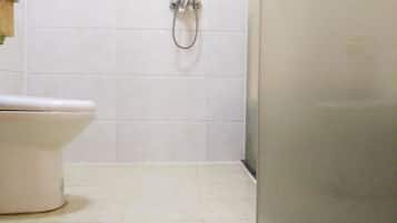 Une salle de bain avec des toilettes, une douche et des murs carrelés.