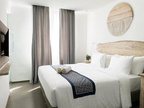 A hotel room with a large bed, two curtains, a round wall decoration, a bedside table with a plant, and a headboard. - Khaiyyara Jimbaran (Ungasan)