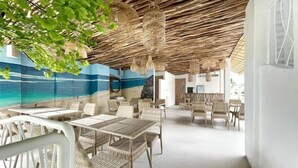 Un restaurante con temática de playa, con mobiliario de mimbre, un mural del océano y lámparas colgantes de mimbre.