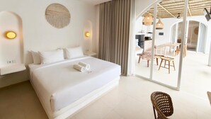 Una habitación de hotel moderna con una cama grande, un comedor con mesa y sillas, y una cocina visible a través de una puerta abierta.