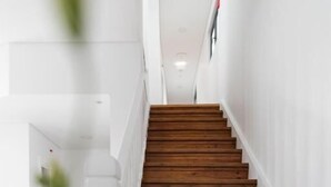 A wooden staircase in a hallway with white walls and a door at the end. - Botica Guesthouse (Espinho)