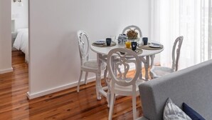 A modern living room with a grey sofa, white chairs, and a round dining table with a hanging light fixture. - Botica Guesthouse (Espinho)