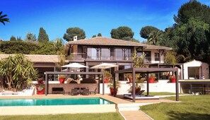 Una casa de dos pisos con piscina, mobiliario exterior y jardín.