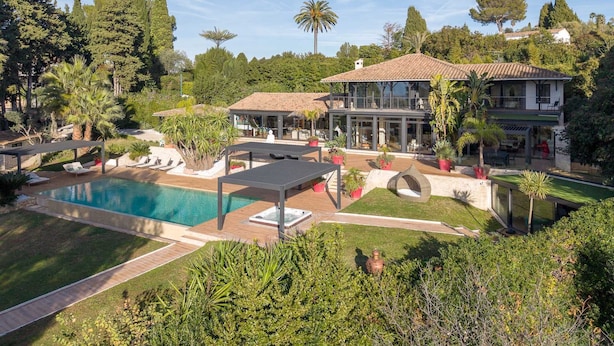 A large house with a swimming pool, outdoor seating, and lush greenery.