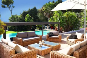 Un espacio al aire libre con muebles de mimbre, piscina y abundante vegetación.