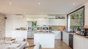 A modern kitchen with a central island, white cabinetry, and a large window with a view of greenery.