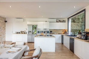 A modern kitchen with a central island, white cabinetry, and a large window with a view of greenery.