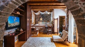 A cozy room with a stone archway, wooden beams, a television, a sofa, a dining table, and a fireplace. - Vasilikata (Lasithi Plateau)