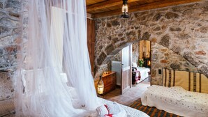 A rustic stone-walled room with a bed, a wooden bench, and a hanging light fixture. - Vasilikata (Lasithi Plateau)