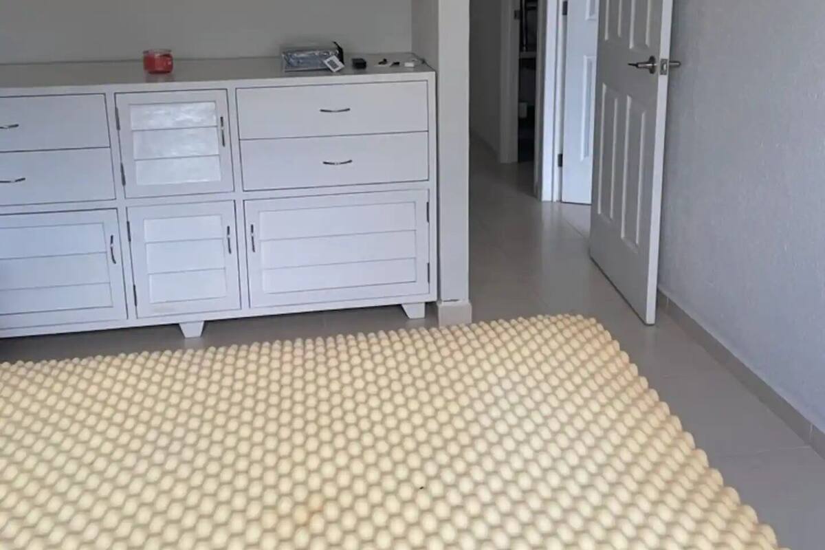 Un dormitorio con un aparador blanco, un televisor montado en la pared y un pasillo que conduce a otra habitación.