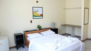 Une chambre d’hôtel avec un lit, un petit bureau, une table de chevet, une lampe, un miroir et un tableau au mur.