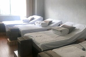 Une chambre d’hôtel avec trois lits, chacun doté de draps et d’oreillers blancs, une fenêtre avec des rideaux et un plancher en bois.
