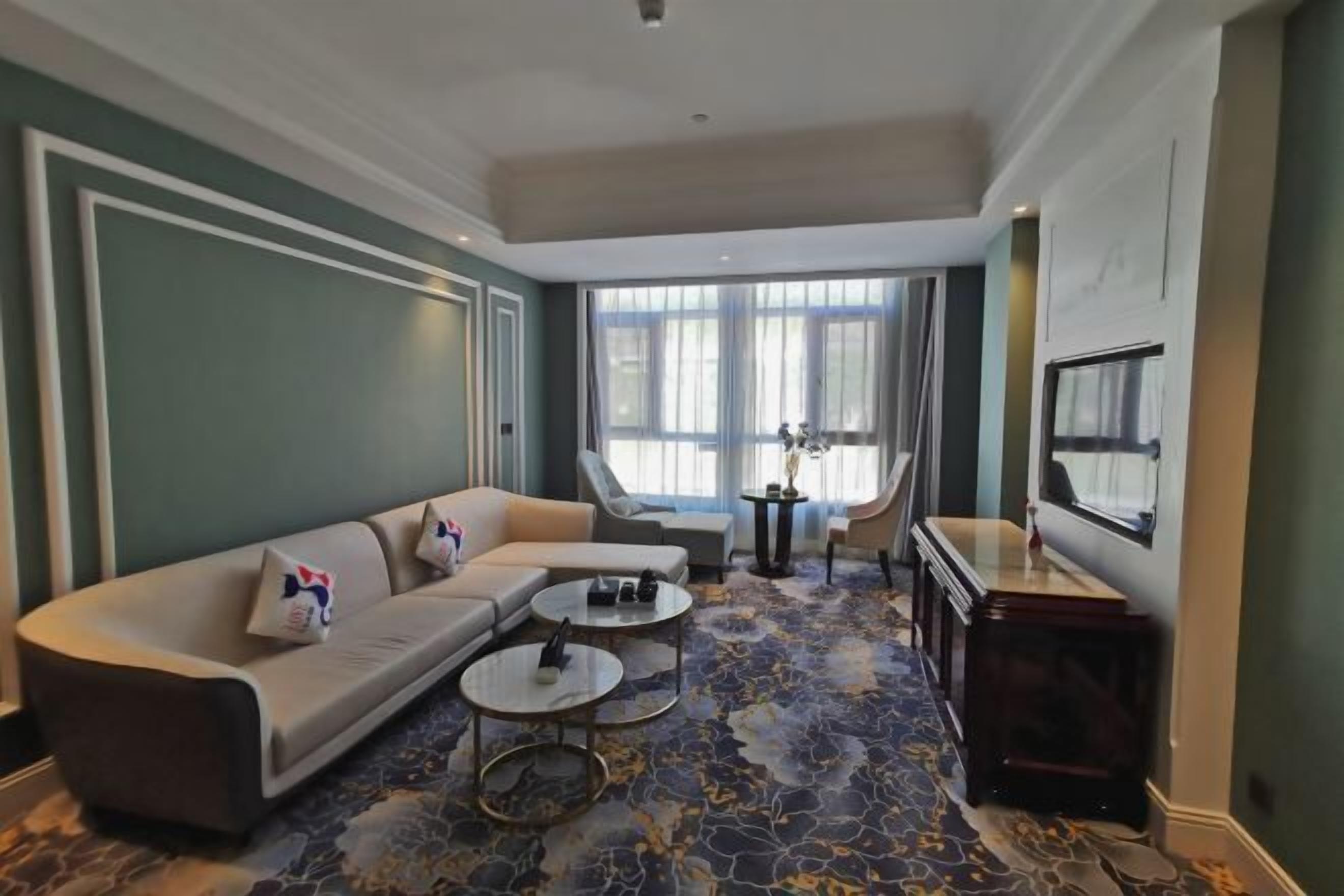 Ein stilvolles Wohnzimmer mit einer gebogenen Couch, zwei runden Couchtischen, einem Beistelltisch und einem großen Fenster mit Vorhängen.