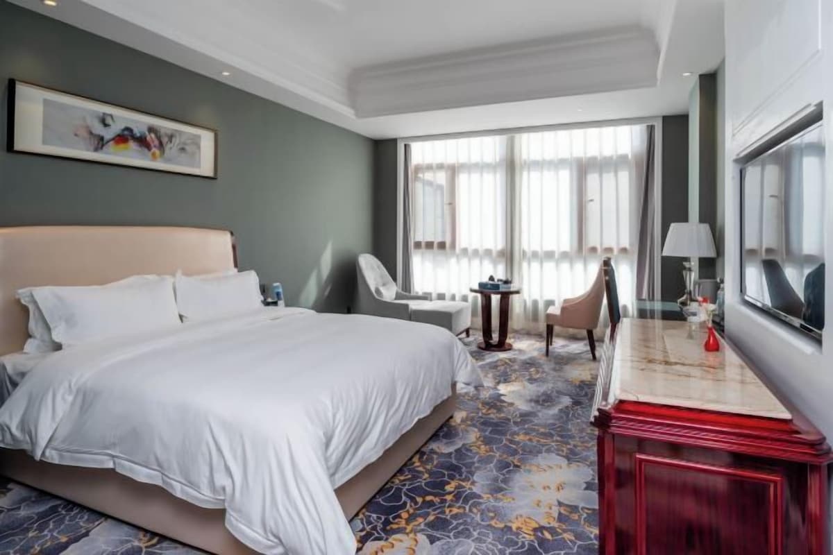 Une chambre d’hôtel avec un grand lit, un bureau avec une lampe, une chaise et une vue sur l’extérieur grâce à de grandes fenêtres.