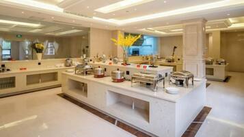 A modern hotel lobby with a central buffet area, a reception desk, and a large mirror reflecting the space.
