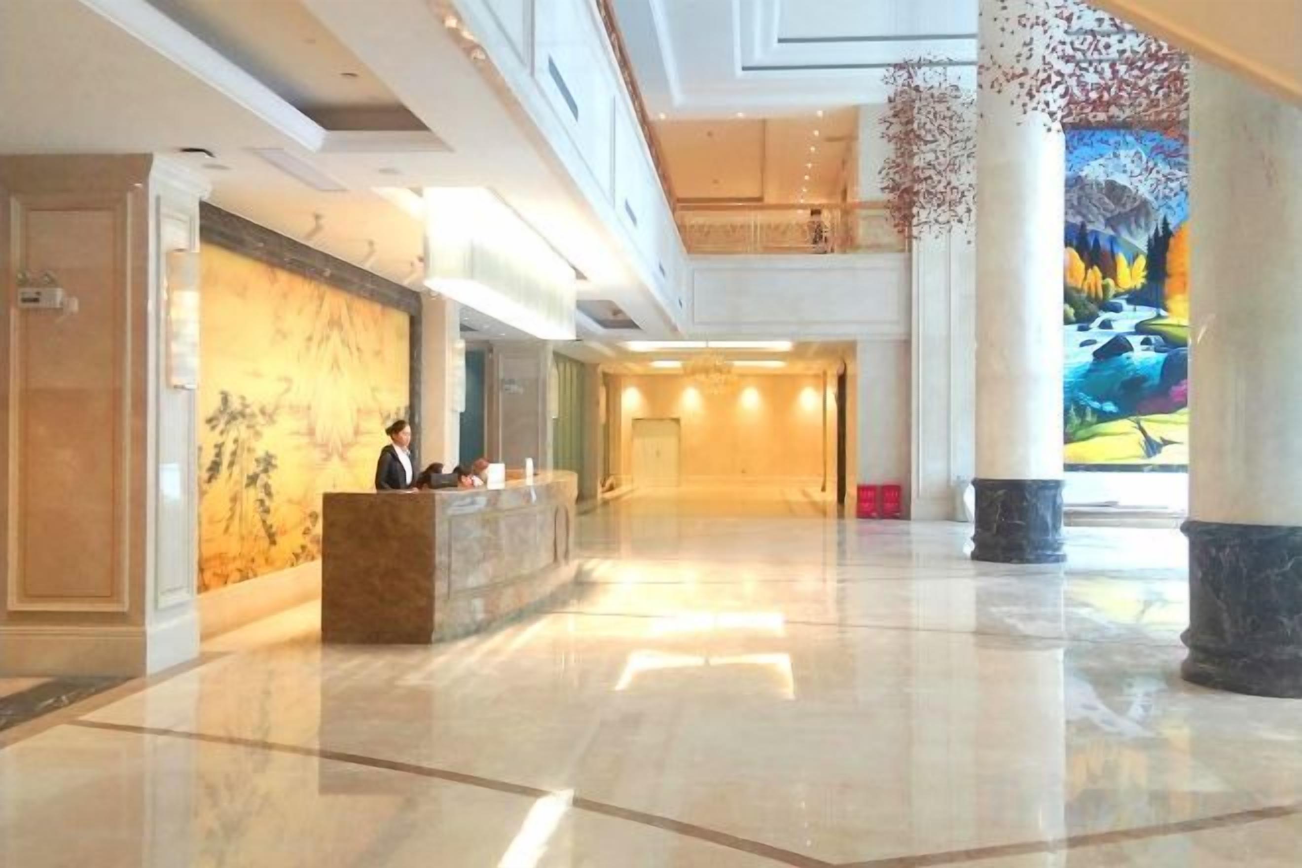 Eine geräumige Lobby mit einer Rezeption, einem großen Wandgemälde und einer hohen Decke.