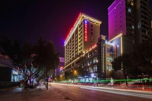 A multi-story hotel with illuminated signage, a wide street in front, and a clear view of the sky. - Nujiang East Wenhao hotel (Lushui)