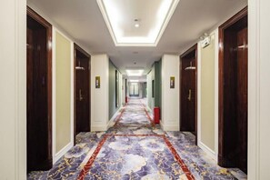 A hotel hallway with a patterned carpet, wooden doors, and a ceiling light fixture. - Nujiang East Wenhao hotel (Lushui)